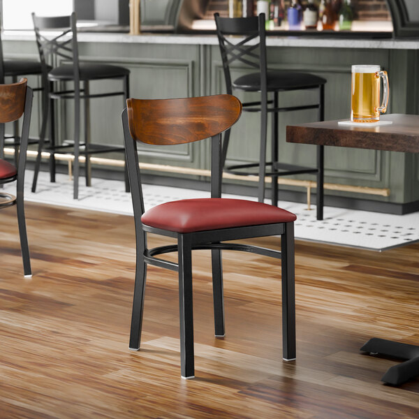A black metal chair with a burgundy vinyl seat and a curved vintage wood backrest.