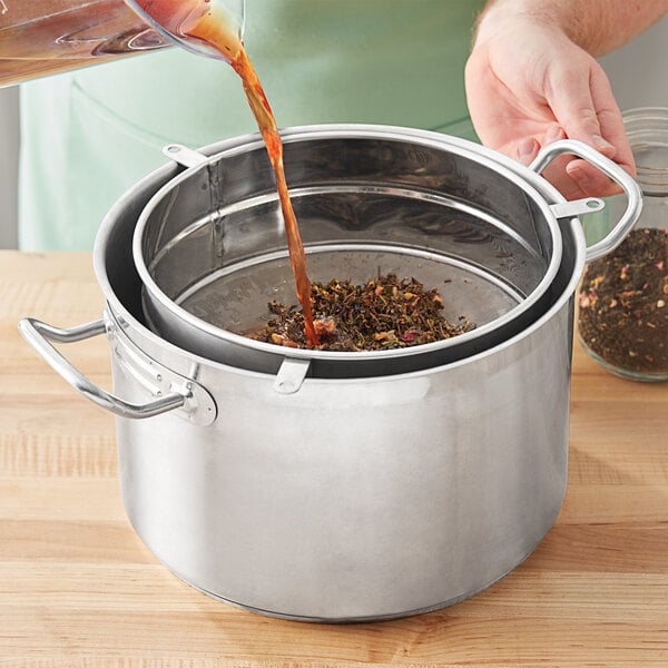 A person pouring liquid into a pot using a Bossen stainless steel mesh tea filter.