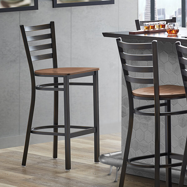 A Lancaster Table & Seating distressed copper ladder back bar stool with a vintage wood seat next to a table.