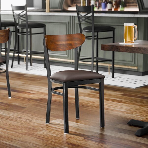 A black metal chair with a dark brown vinyl seat and a curved vintage wood backrest.