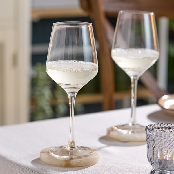 Two Acopa Silhouette wine glasses filled with white liquid on a table.