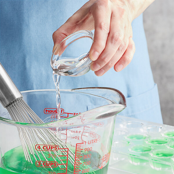 A person using LorAnn Tart and Sour Flavor Booster to mix a green liquid with a whisk in a glass bowl.