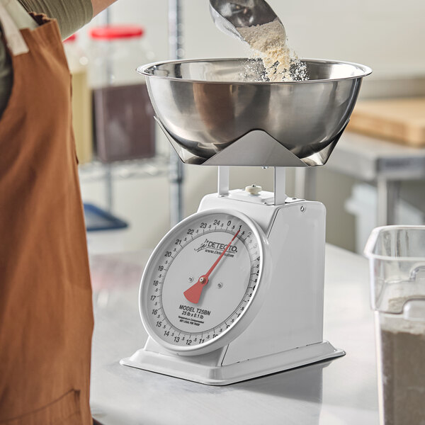 A mechanical portion control dial scale with a stainless steel bowl being used to measure ingredients.