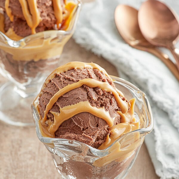 A bowl of ice cream topped with peanut butter sauce next to a spoon.