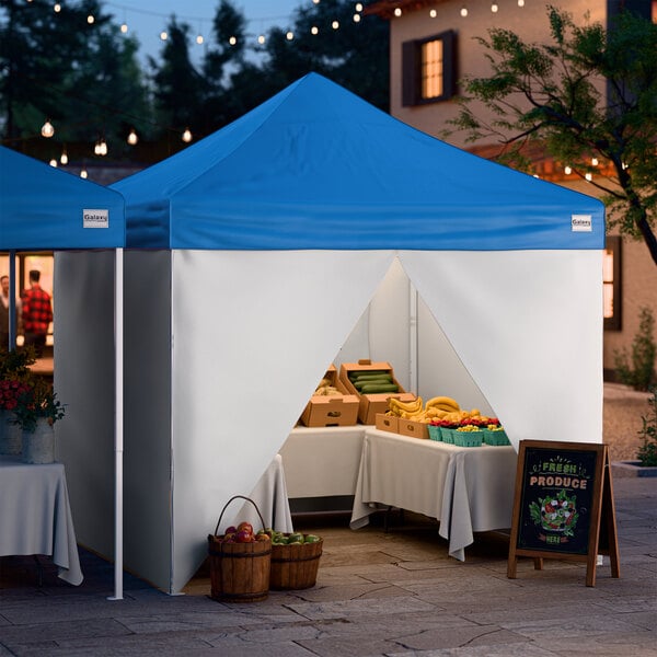 A blue and white 10' x 10' pop-up canopy tent with straight legs and four side walls, set up as a market stall.