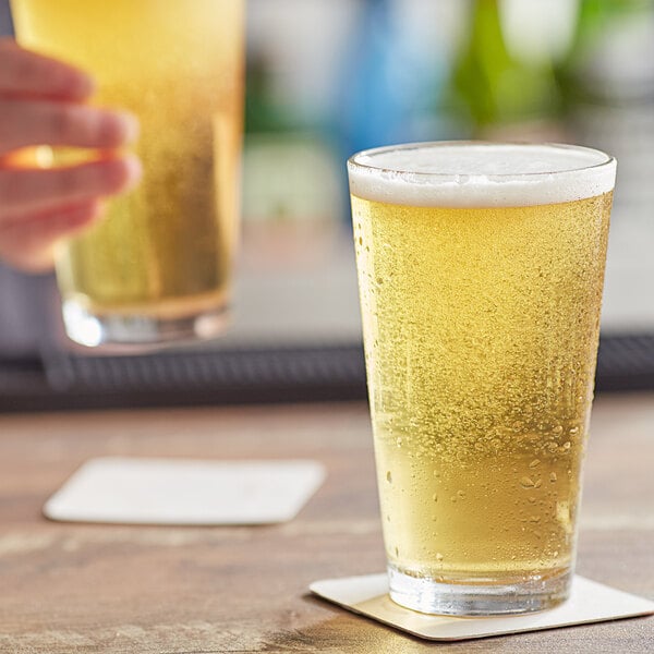 A person holding an Arcoroc ArcoPrime pint glass of beer with bubbles.