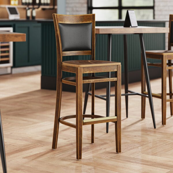 A Lancaster Table & Seating Sofia wood bar stool with a vintage wood seat at a table in a restaurant.