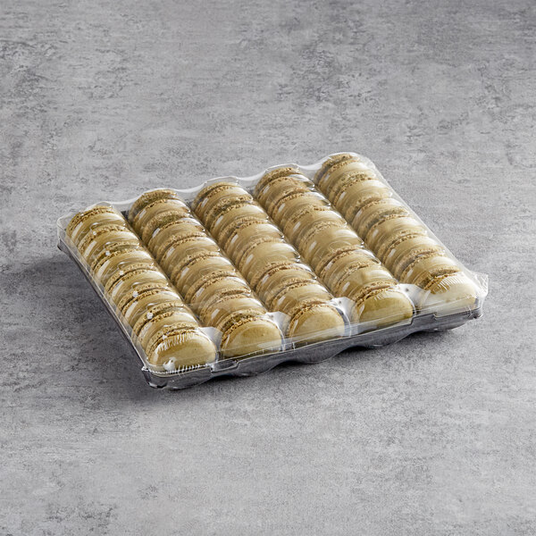 A tray of White Toque French pistachio macarons in plastic wrap on a gray surface.