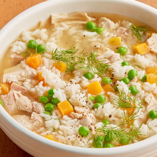 A bowl of chicken and Riceland Oriental Style Long Grain White Rice soup with peas and carrots.