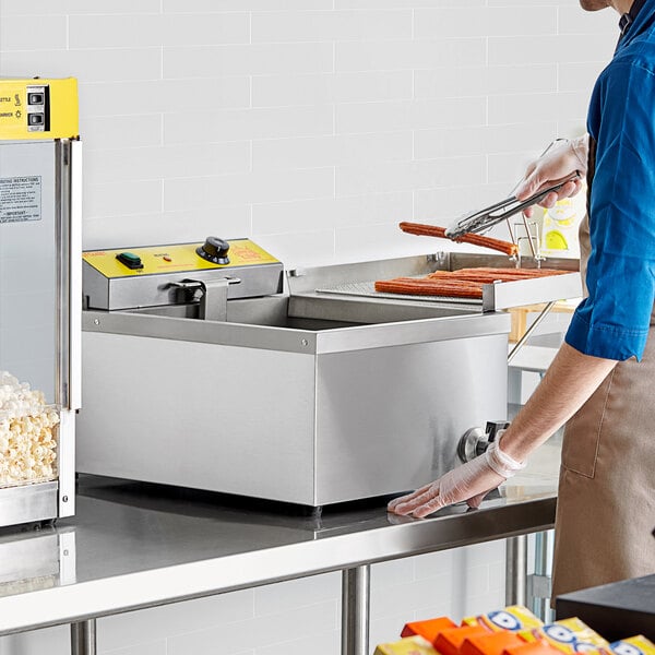 A man in a blue shirt and apron using a Carnival King funnel cake fryer.