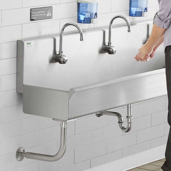 A man standing in front of a Regency stainless steel multi-station hand sink.