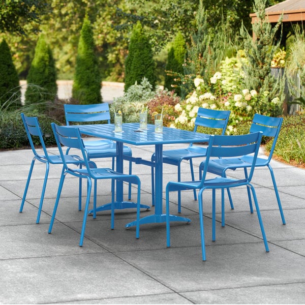 A blue Lancaster Table & Seating outdoor dining table with blue chairs on a concrete patio.