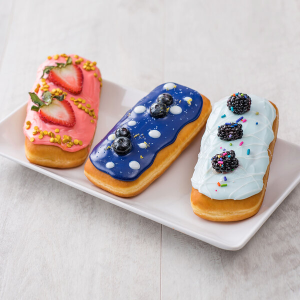 A plate of Rich's unfilled long john yeast donuts with colorful sprinkles and berries.