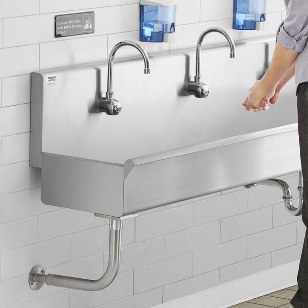 A person standing in front of a Regency stainless steel multi-station hand sink.