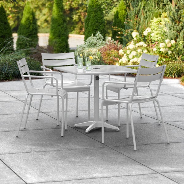 A Lancaster Table & Seating outdoor dining set with white chairs on a patio.