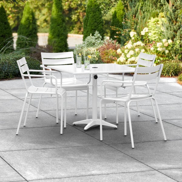 A white table with umbrella hole and 4 chairs on a patio.