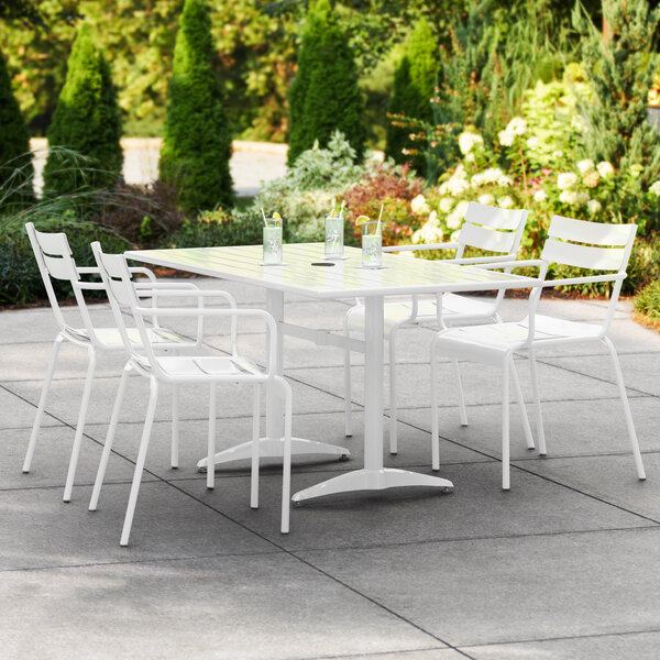 A white Lancaster Table & Seating outdoor dining table with four white arm chairs on a patio.