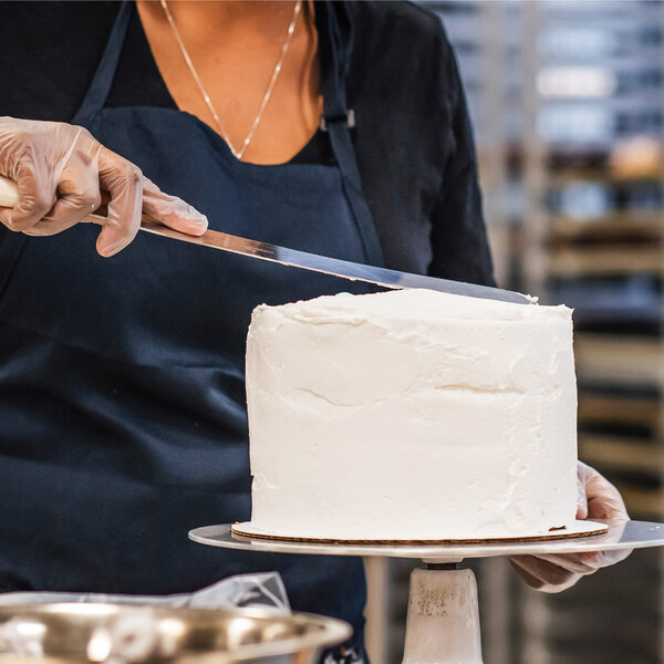 A woman in a black apron using a knife to cut a cake with Rich's Bettercreme Vanilla Whipped Icing on it.