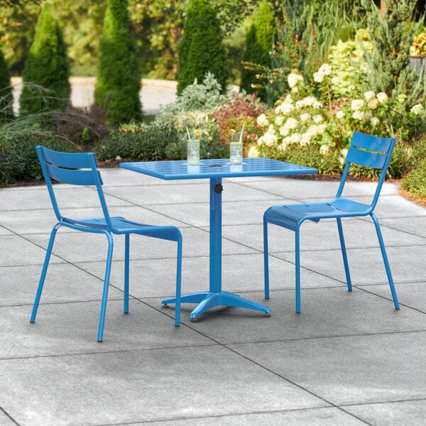 A blue table and chairs on a stone patio with an umbrella.