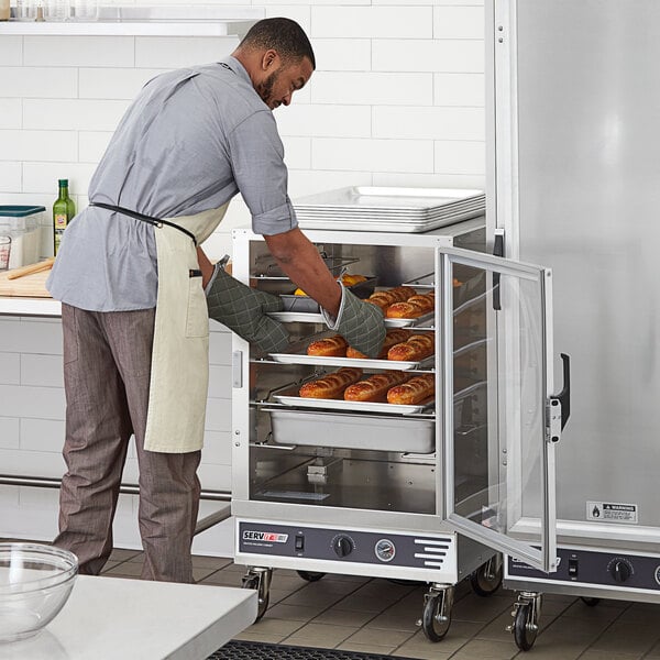 A man putting food in a ServIt holding cabinet with a clear door.