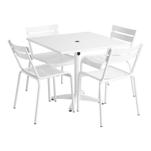 A white Lancaster Table & Seating outdoor table with a round hole and four white chairs.