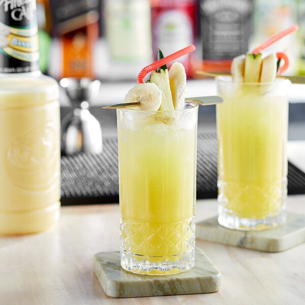 Two glasses of Finest Call banana drinks with fruit on top on a marble coaster.