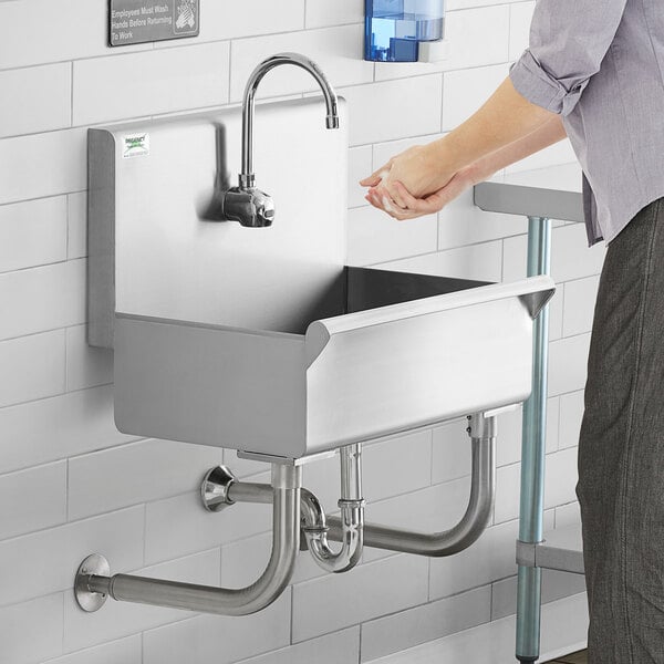 A person washing their hands in a Regency hand sink with hands-free faucet.