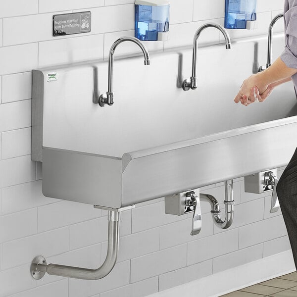 A man standing next to a Regency wall-mounted utility sink with knee-operated faucets.