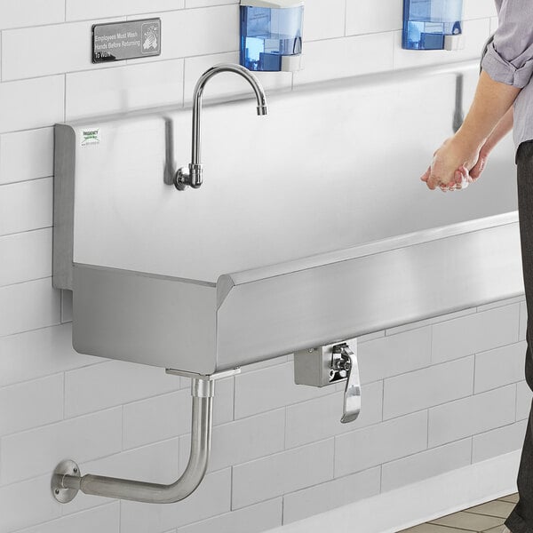 A man standing near a Regency stainless steel multi-station hand sink.