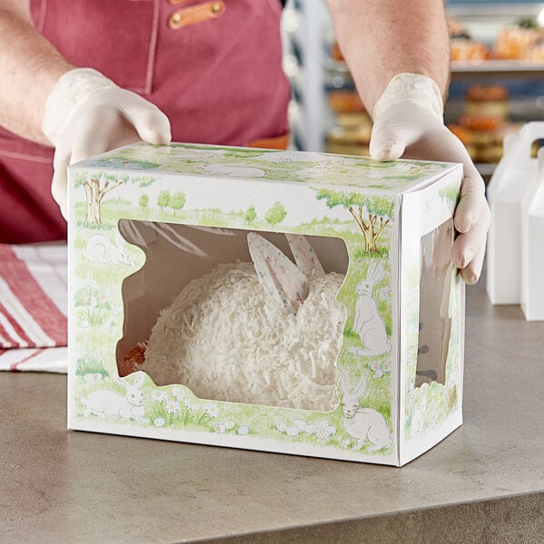 A person wearing gloves holding a Southern Champion bakery box with a bunny inside.