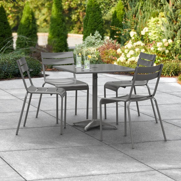 A Lancaster Table & Seating matte gray aluminum outdoor dining table with chairs and an umbrella on a patio.