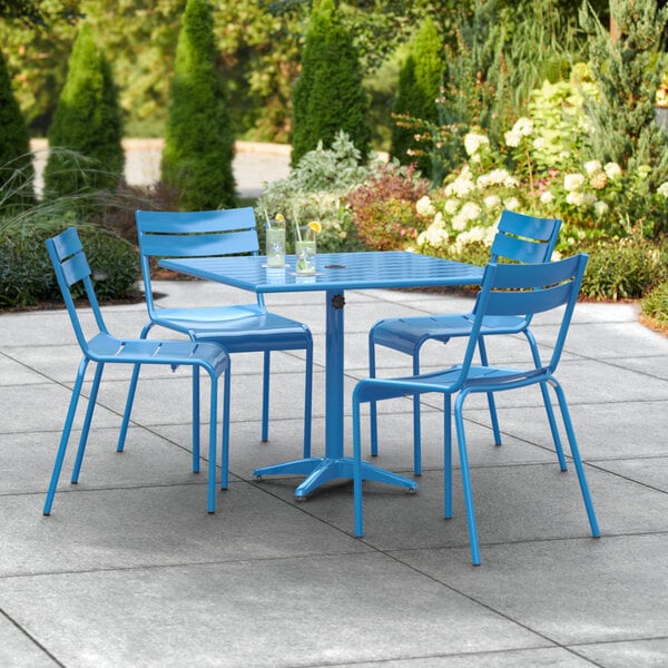 A blue Lancaster Table & Seating dining height outdoor table and 4 chairs on a concrete patio.