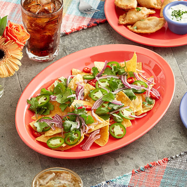 An Acopa orange melamine platter of nachos with jalapenos and onions on a table.