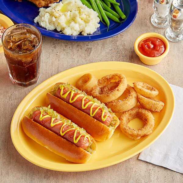 A yellow oval platter with hot dogs, onion rings, green beans, and mashed potatoes on it.