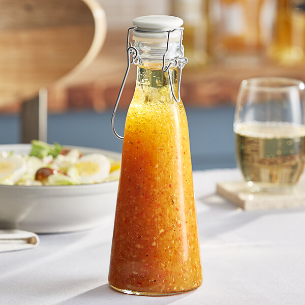 A Tablecraft glass carafe filled with orange sauce on a table.