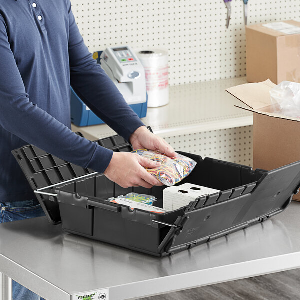 A man putting a black Lavex storage box with an attached lid into a stack of black storage boxes.