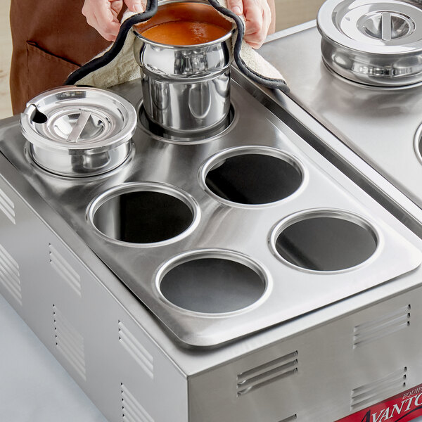 A woman using a ServIt steam table adapter plate with holes to pour liquid into a pot.