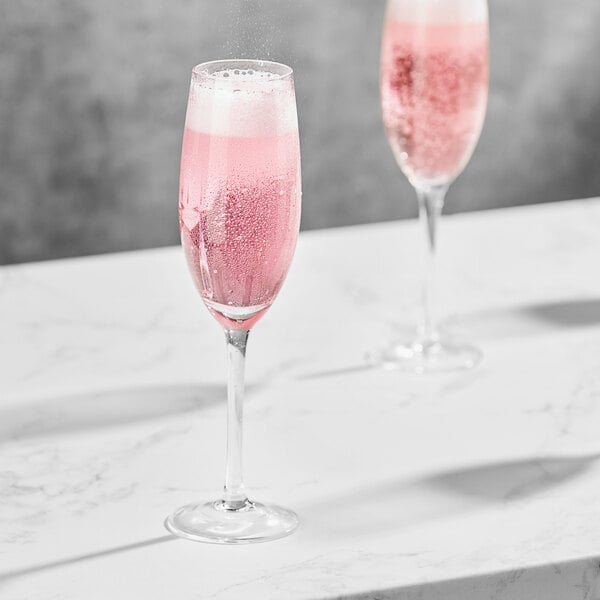 Two Della Luce Maia flute glasses filled with pink liquid on a white table.