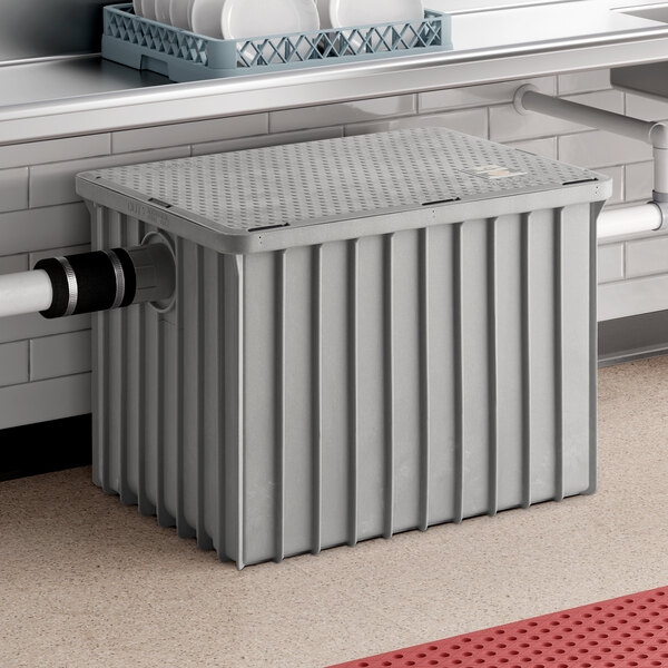 A large gray Endura grease trap with a ribbed exterior and 3-inch threaded pipe connections, installed under a commercial kitchen sink.