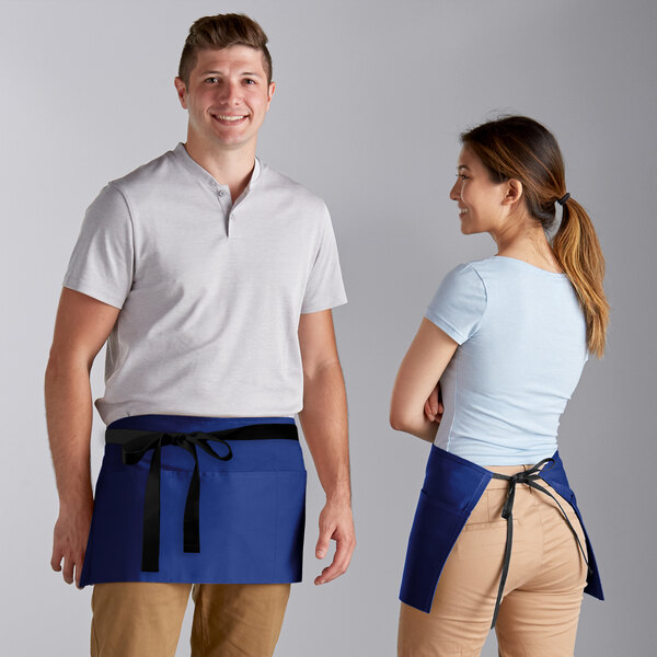 A man and woman standing on a professional kitchen wearing blue Choice waist aprons with black webbing.