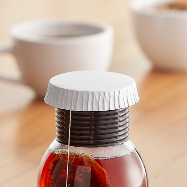 A glass of tea with a white 2 1/2" Disposable Hottle Cap on a table.