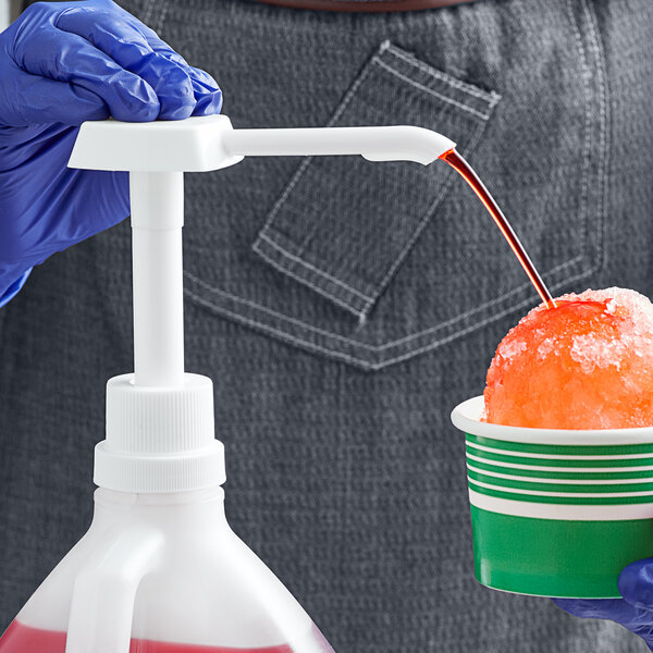A gloved hand uses a white plastic Carnival King condiment pump to pour liquid into a bowl of snow.