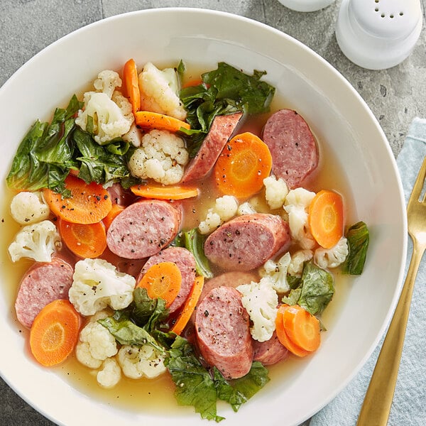 A bowl of soup with carrots, cauliflower, and sliced Warrington Farm Meats Smoked Kielbasa sausage.