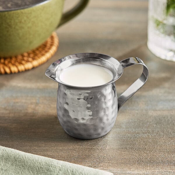 A Vollrath stainless steel bell creamer with white liquid in it.