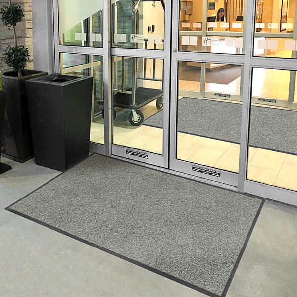 A door with glass doors open to reveal a gray Lavex Plush Dilour entrance mat.