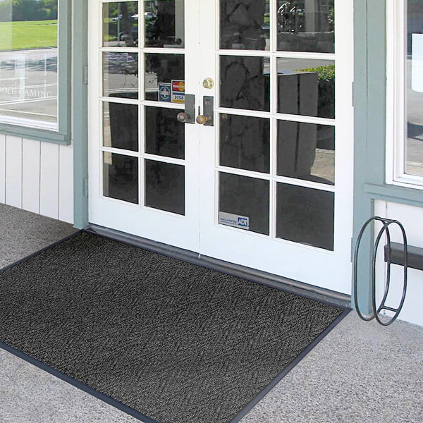A black Lavex Chevron Rib indoor entrance mat on a white door.