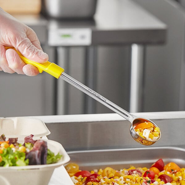 A person holding a Choice yellow solid portion spoon filled with food over a bowl.