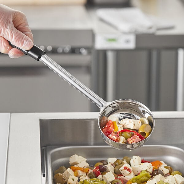 A hand holding a black perforated portion spoon with food in it.