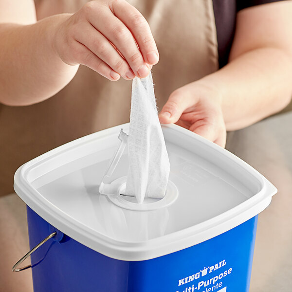 A person putting a tissue into a white Noble Products plastic lid on a blue container.