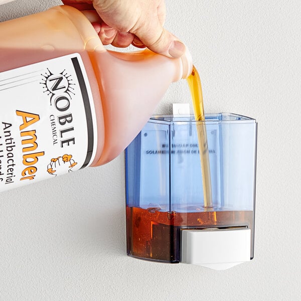 A hand pouring brown liquid into a soap dispenser.